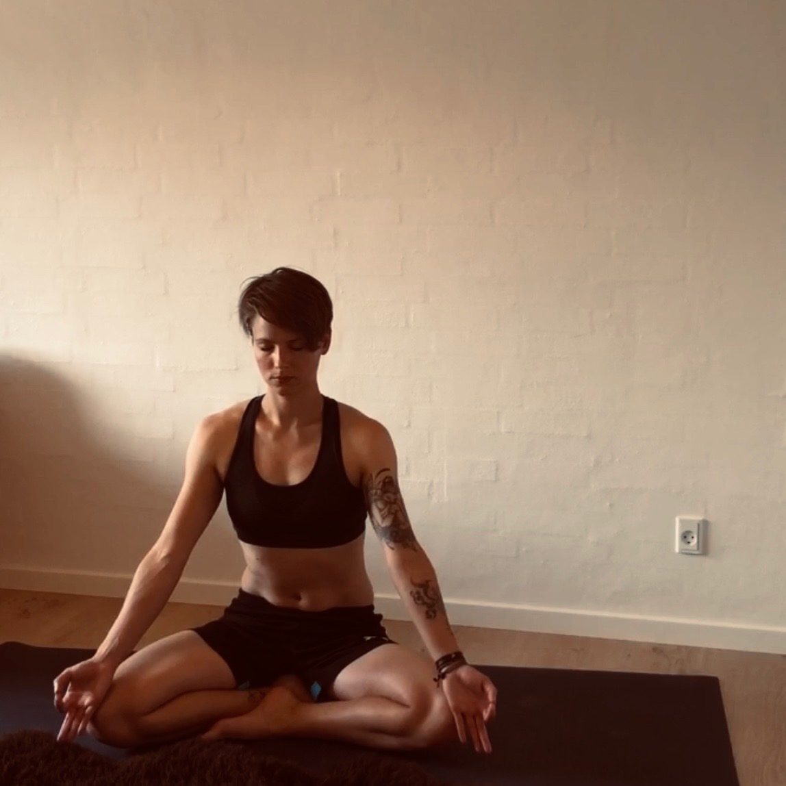 Sillan sidder i skrædderstilling og mediterer på en yogamåtte.